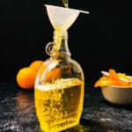 orange simple syrup being poured into a glass jar.