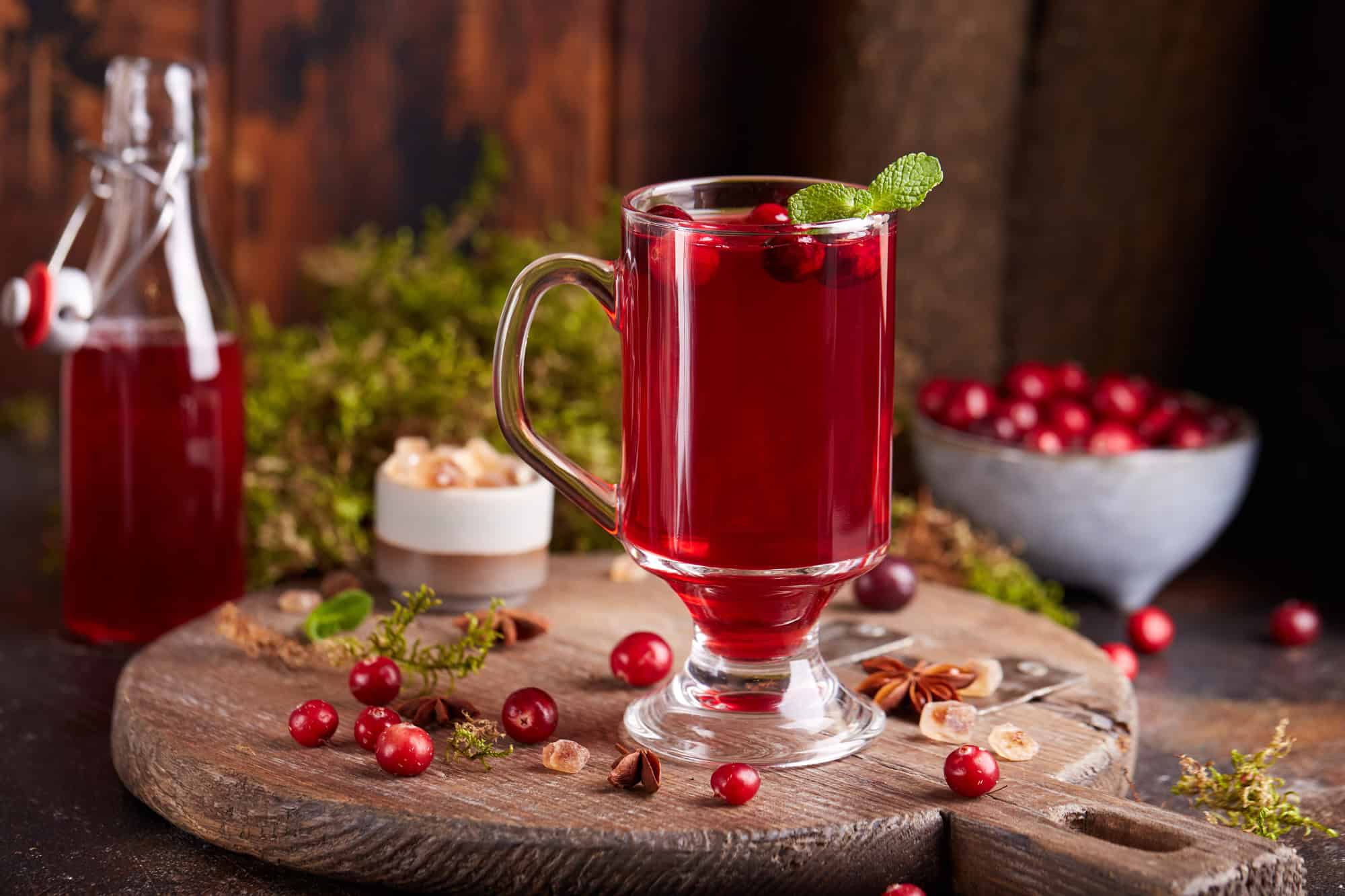 A glass with cranberry mors surrounded by cranberries