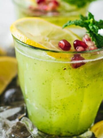Two glasses of lemonade with pomegranate seeds, mint and lemon slices.