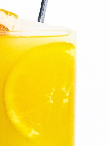 A glass of orange juice with a slice of orange on the rim and a slice of grapefruit on top, against a white background.