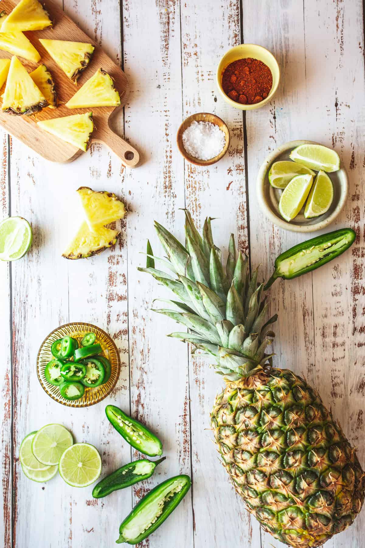 A pineapple, limes, jalapeos and other ingredients on a wooden table.