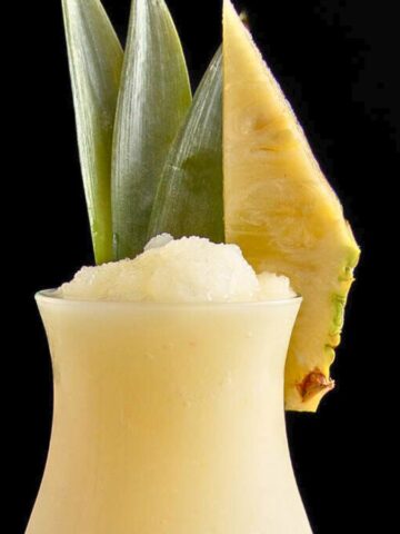 A glass with a drink and a slice of pineapple.
