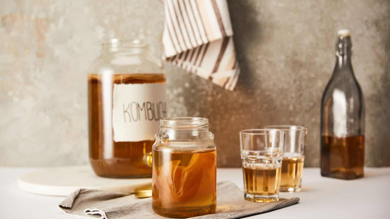 A kitchen countertop displays a glass jar, two glasses, and a bottle of kombucha