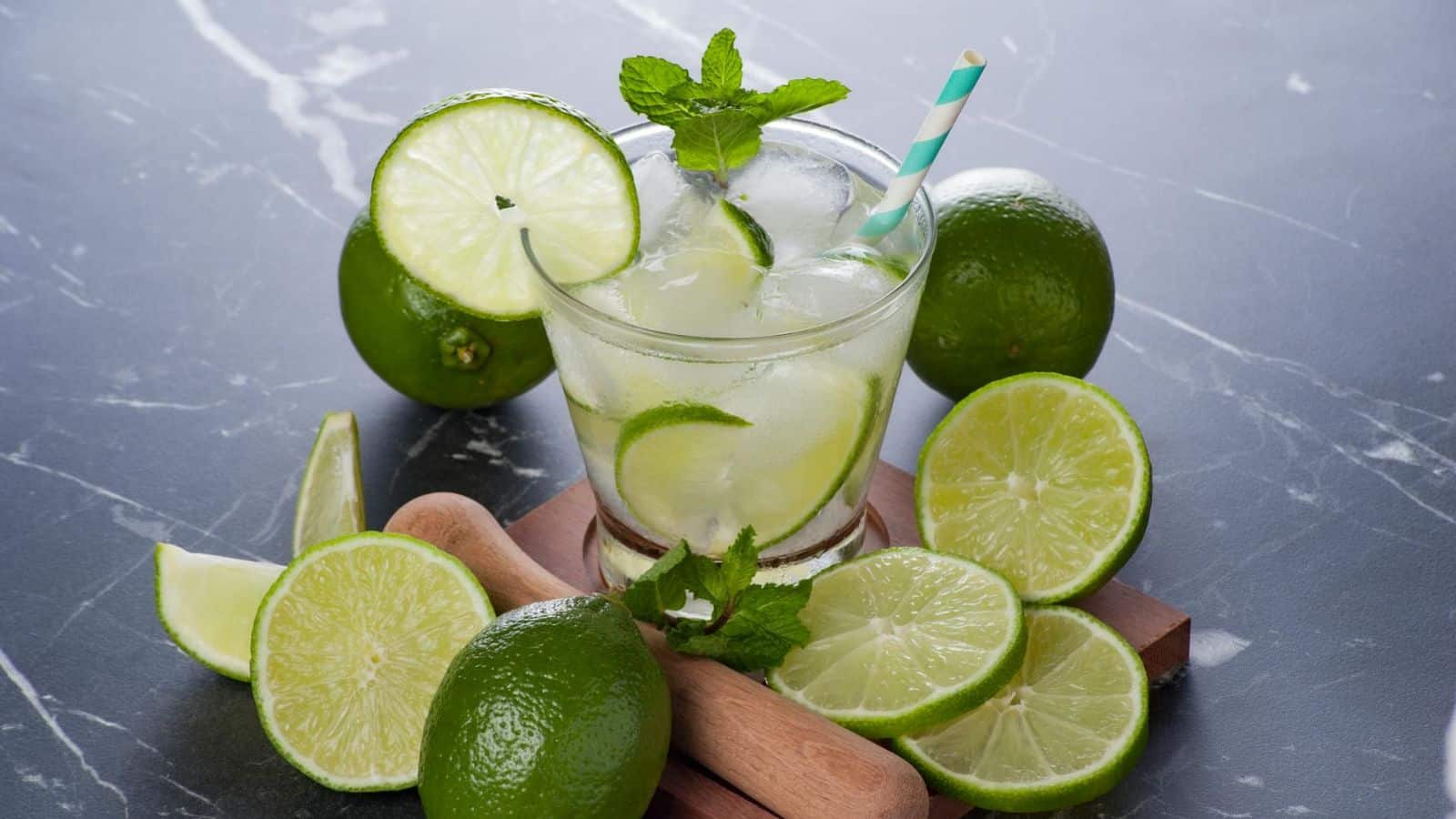 A glass of Caipirinha surrounded by sliced limes