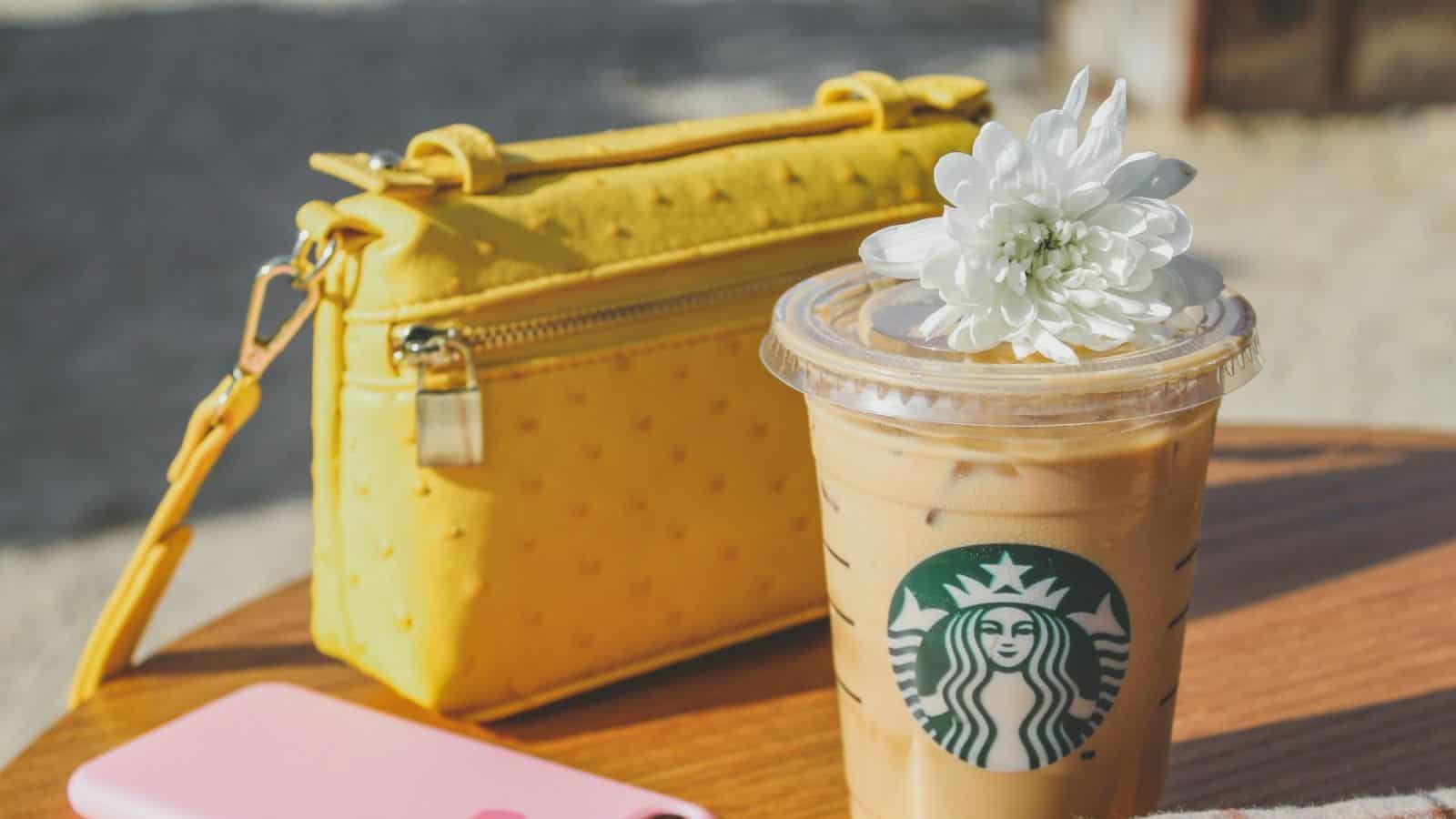 Plastic Starbucks cup with coffee placed on table with a bag and a phone on the background