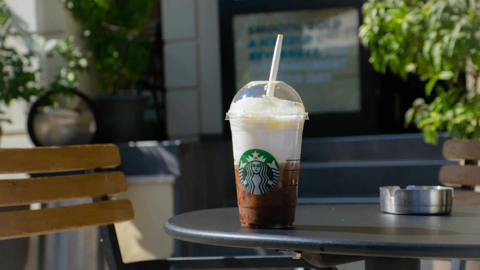 Plastic Starbucks cup filled with foamy coffee on top of table outdoors