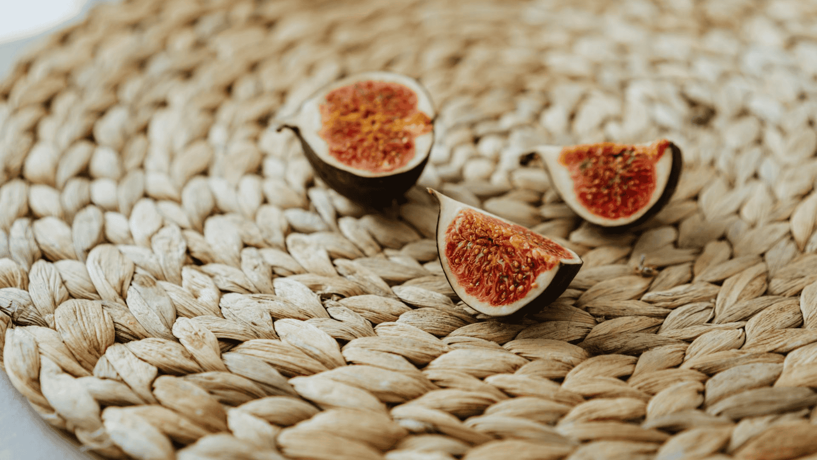 Three pieces of sliced fig, reminiscent of the rare flavors found in unusual plants for winemaking, are placed on a woven straw placemat.