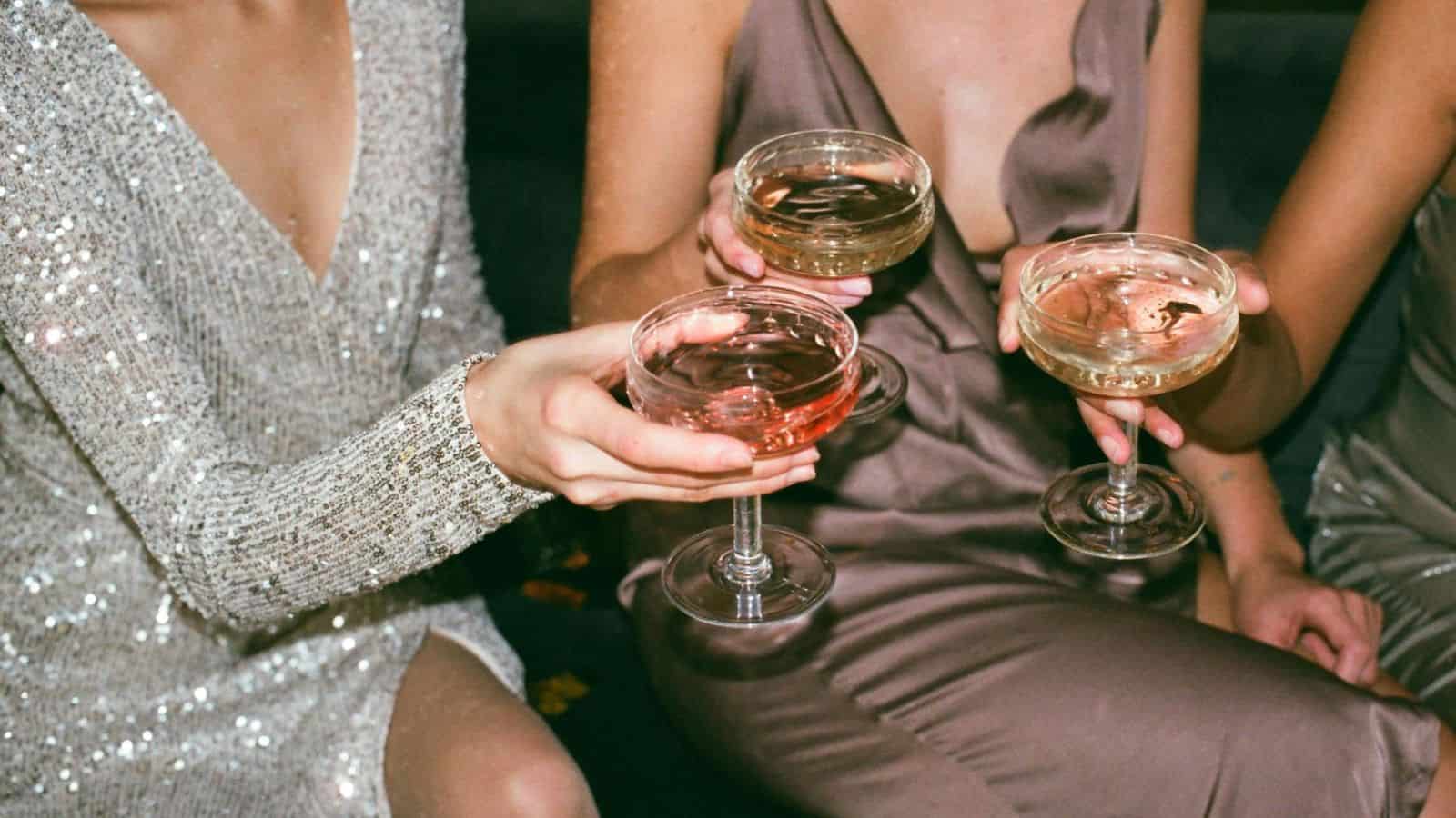 Three women in dresses toast their champagne glasses