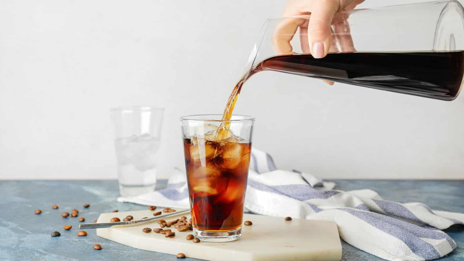Hand pouring iced americano onto a glass filled with ice