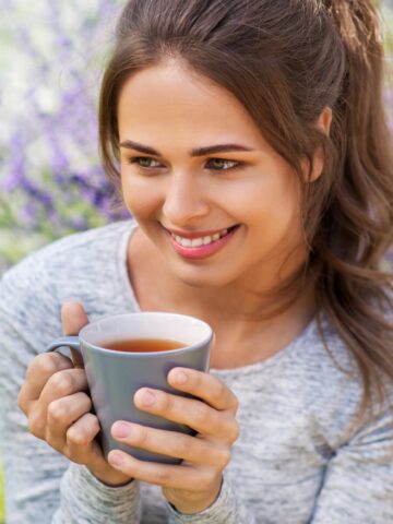 Woman holding cup of tea in front of lilac bush.