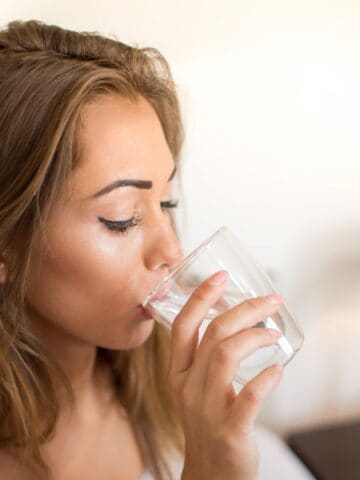 Woman drinking a glass of water while sitting on her bed