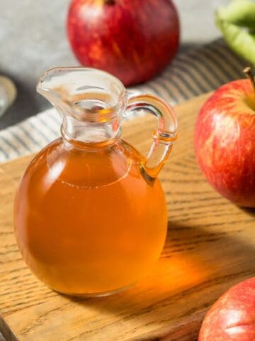 Apple cider vinegar on a chopping board with apples in the background