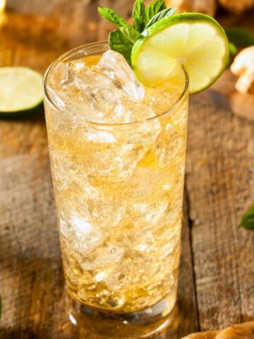 Two glasses of sparkling ginger ale garnished with lime and slices of lime and ginger in the background