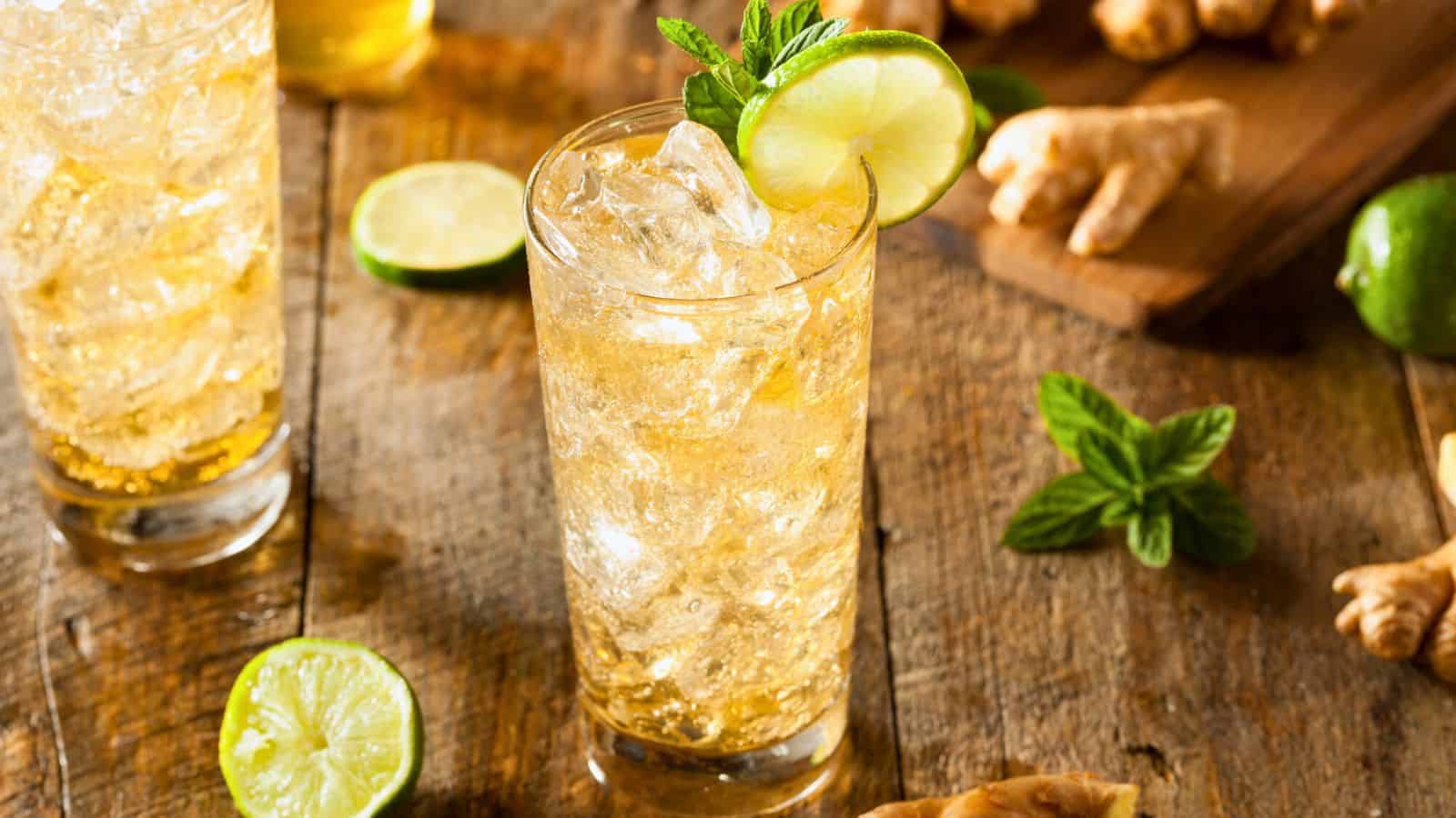 Two glasses of sparkling ginger ale garnished with lime and slices of lime and ginger in the background