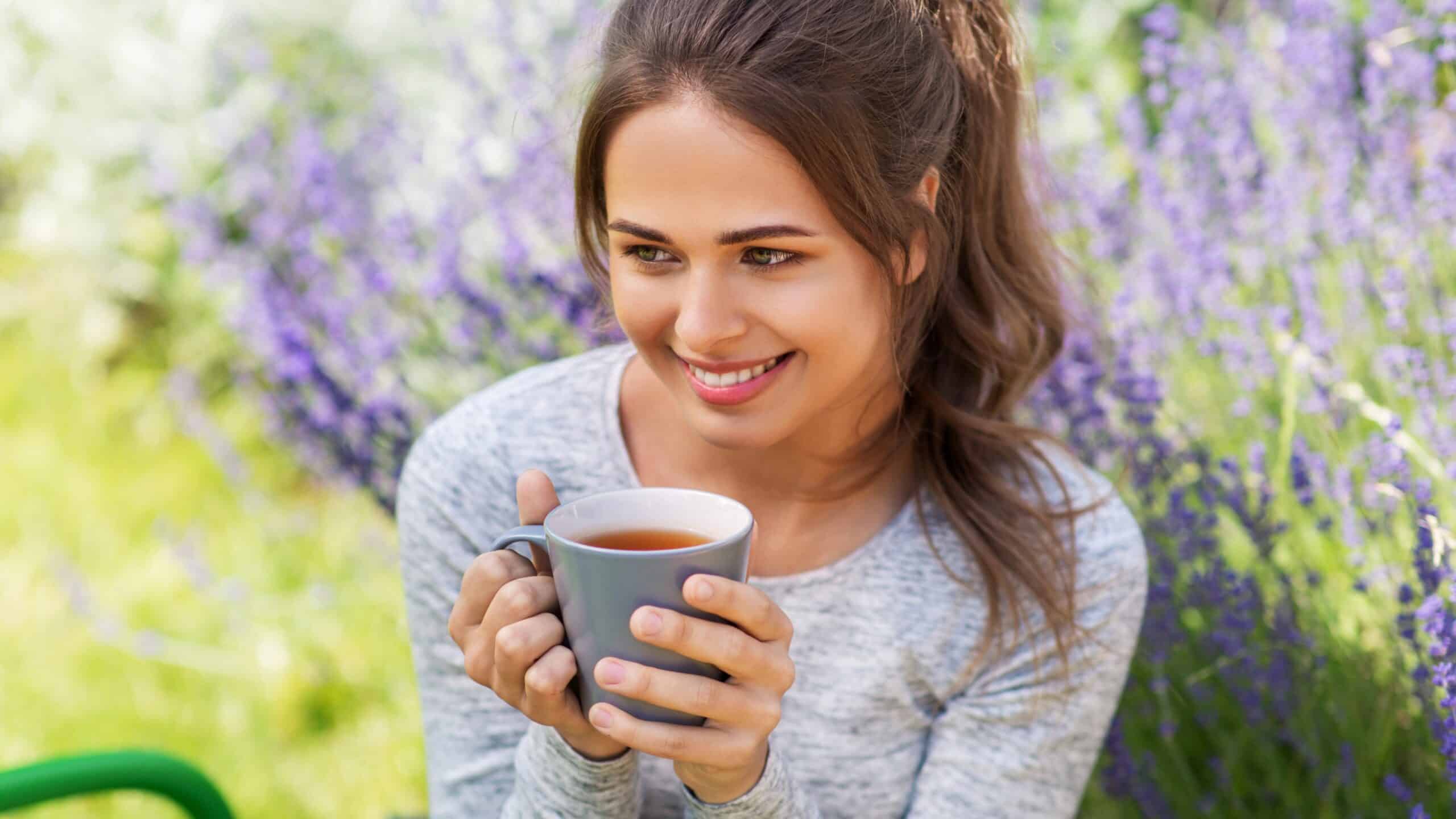 Woman holding cup of tea in front of lilac bush.