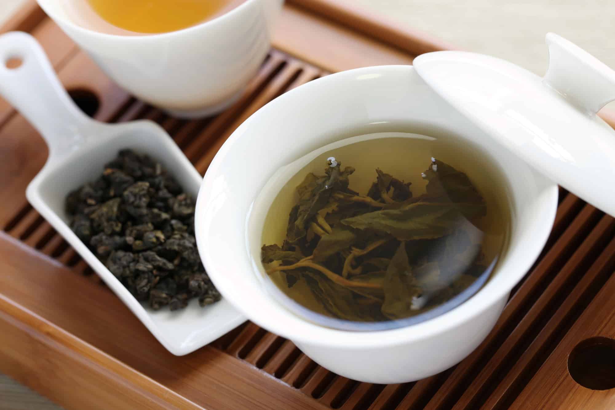 Cup of oolong tea with more tea leaves besides.