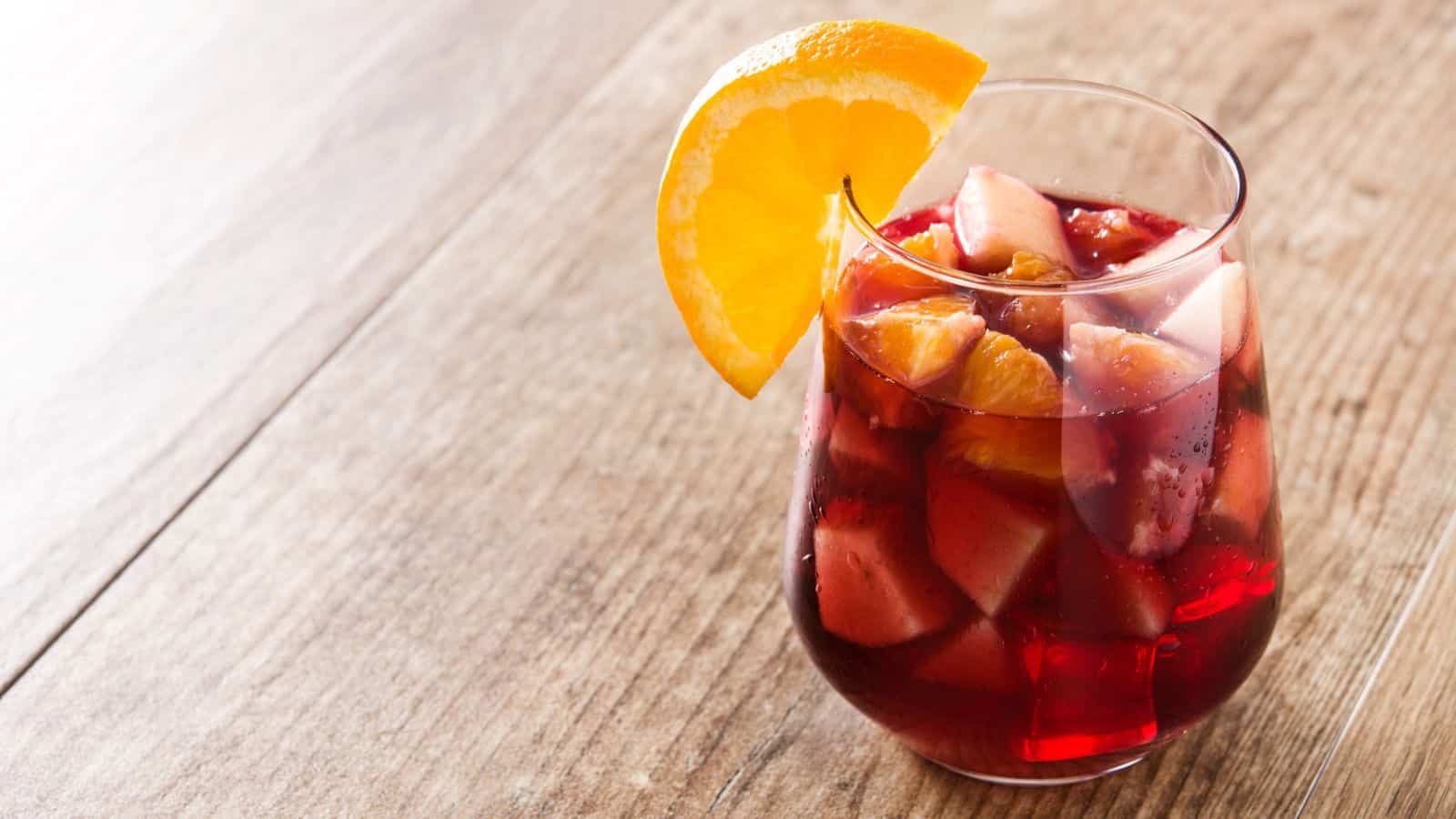A glass of sangria garnished with a piece of orange on top of a table