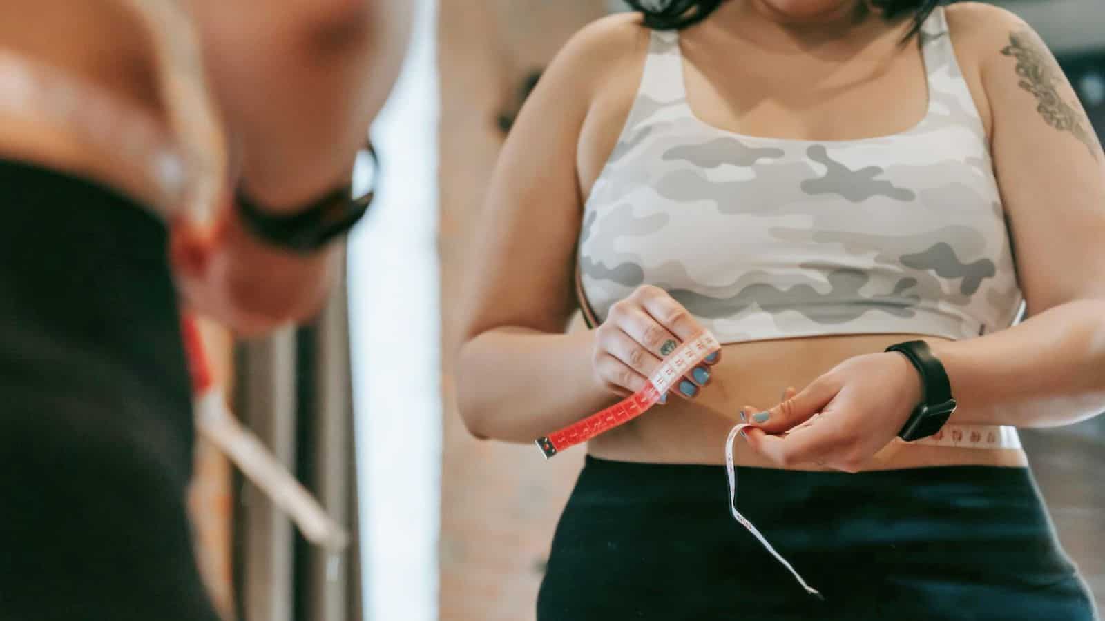 A person measuring her waist size with tape measure in front of a mirror.
