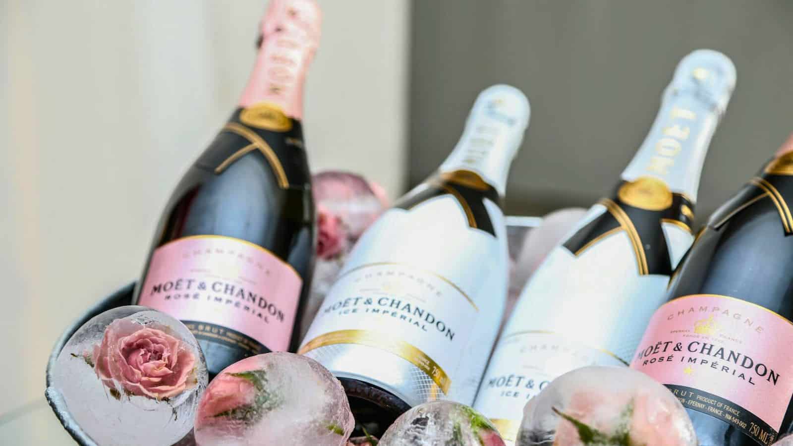 Four bottles of Moët & Chandon Ice Impérial champagne, two with pink labels and two with white labels, are displayed in a bucket filled with ice and decorative frozen roses—just remember, indulging in such alcoholic drinks that are bad for your teeth might make their beauty bittersweet!