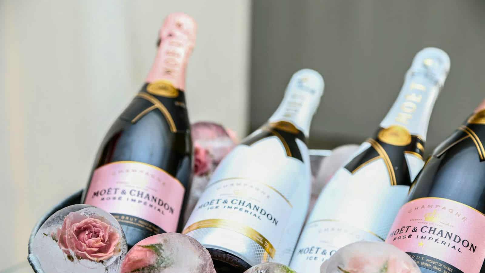 A close-up of four bottles of Mo&euml;t & Chandon champagne placed in an ice container. Two bottles have a pink label (Ros&eacute; Imp&eacute;rial), and two have a white label with gold accents (Ice Imp&eacute;rial). The ice includes frozen flowers, showcasing types of alcohol you should savor responsibly.