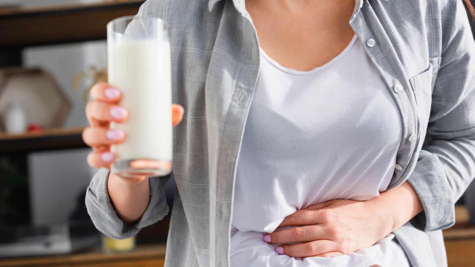 Woman clutching her stomach while holding a glass of milk