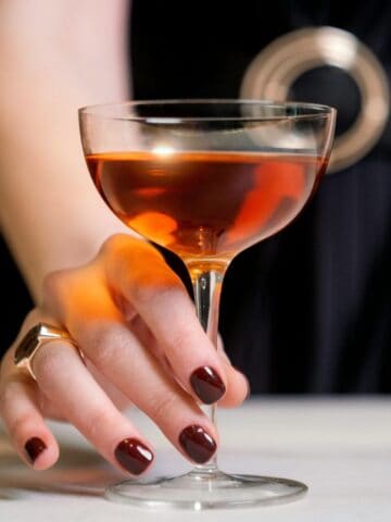 Person with burgundy nail polish holds a flute filled with alcohol