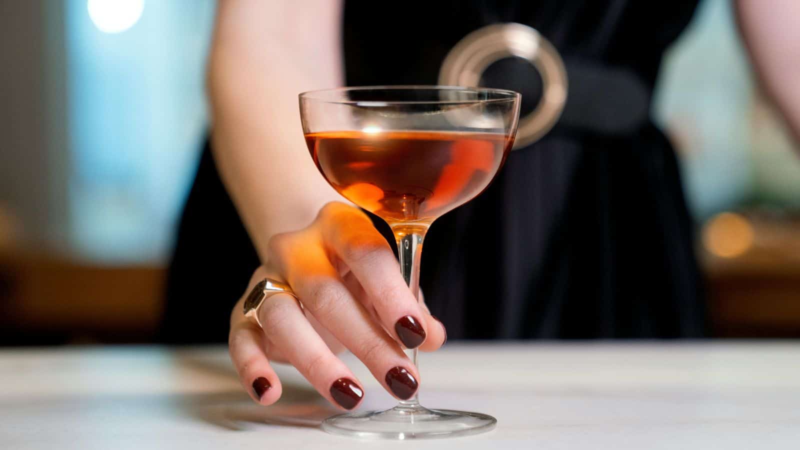 Person with burgundy nail polish holds a flute filled with alcohol
