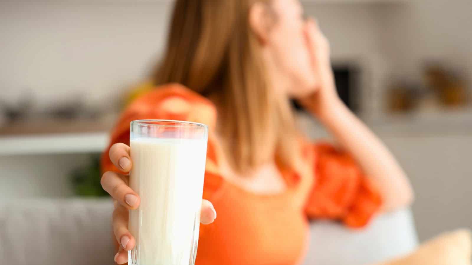A woman gagging and facing away while holding a glass of milk