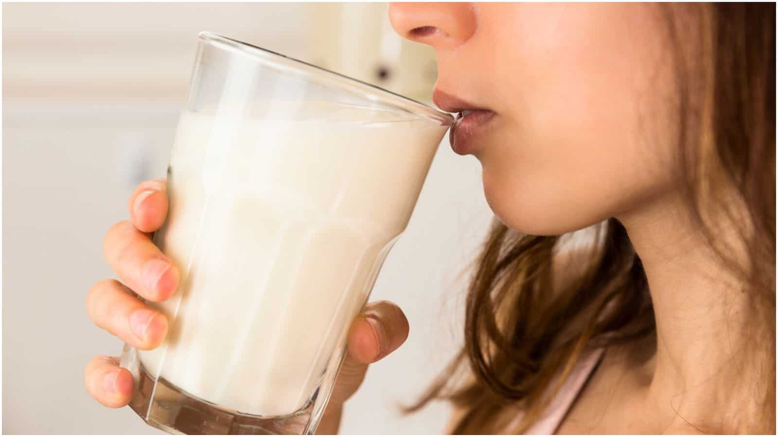 Close-up image of a person drinking milk from a clear glass. The person is holding the glass with their right hand, savoring one of the recommended drinks for gout relief. The background is slightly blurred, highlighting the freshness of the milk.