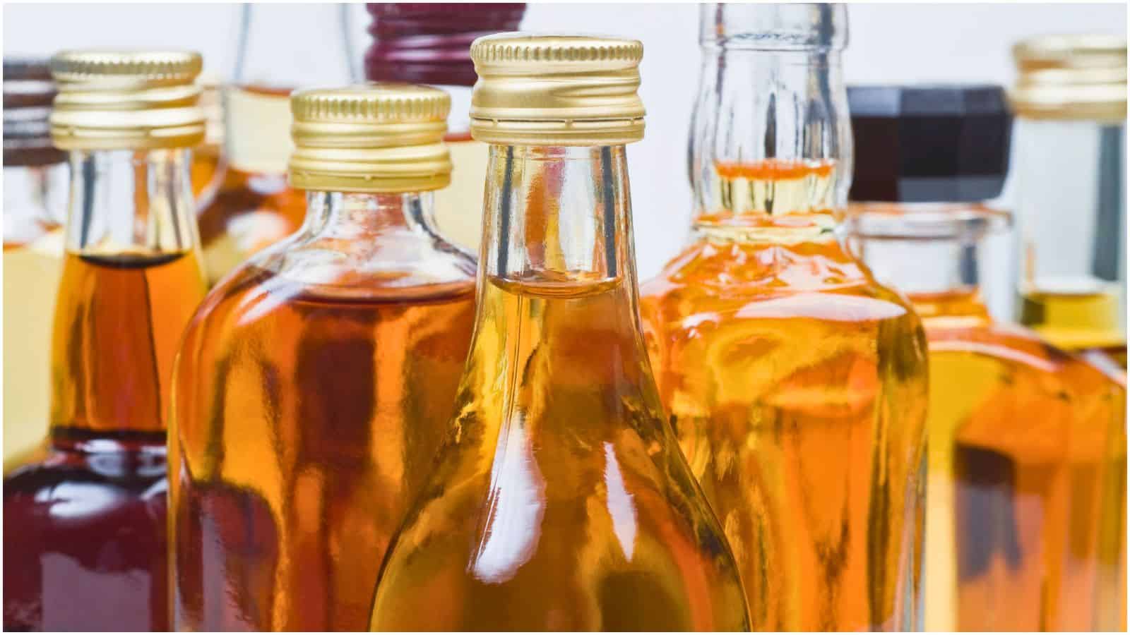 A close-up image of various glass bottles filled with different types of amber-colored liquids. Some bottles have gold screw caps, while others have clear or colored tops. The liquids inside range from light to dark amber hues, reminiscent of the types of alcohol you shouldn't be drinking.