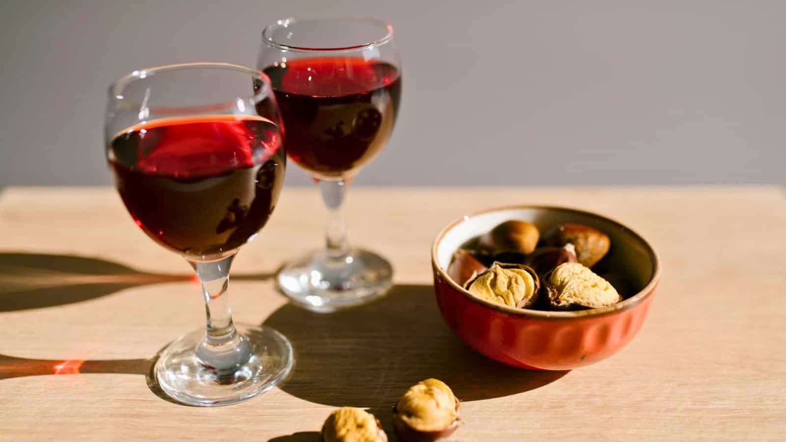 Two glasses filled with red wine and a bowl of snacks beside them