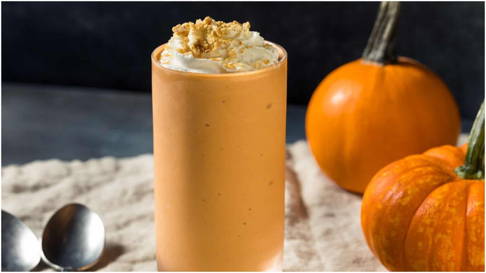 A tall glass of pumpkin seed milkshake with pumpkins in the background