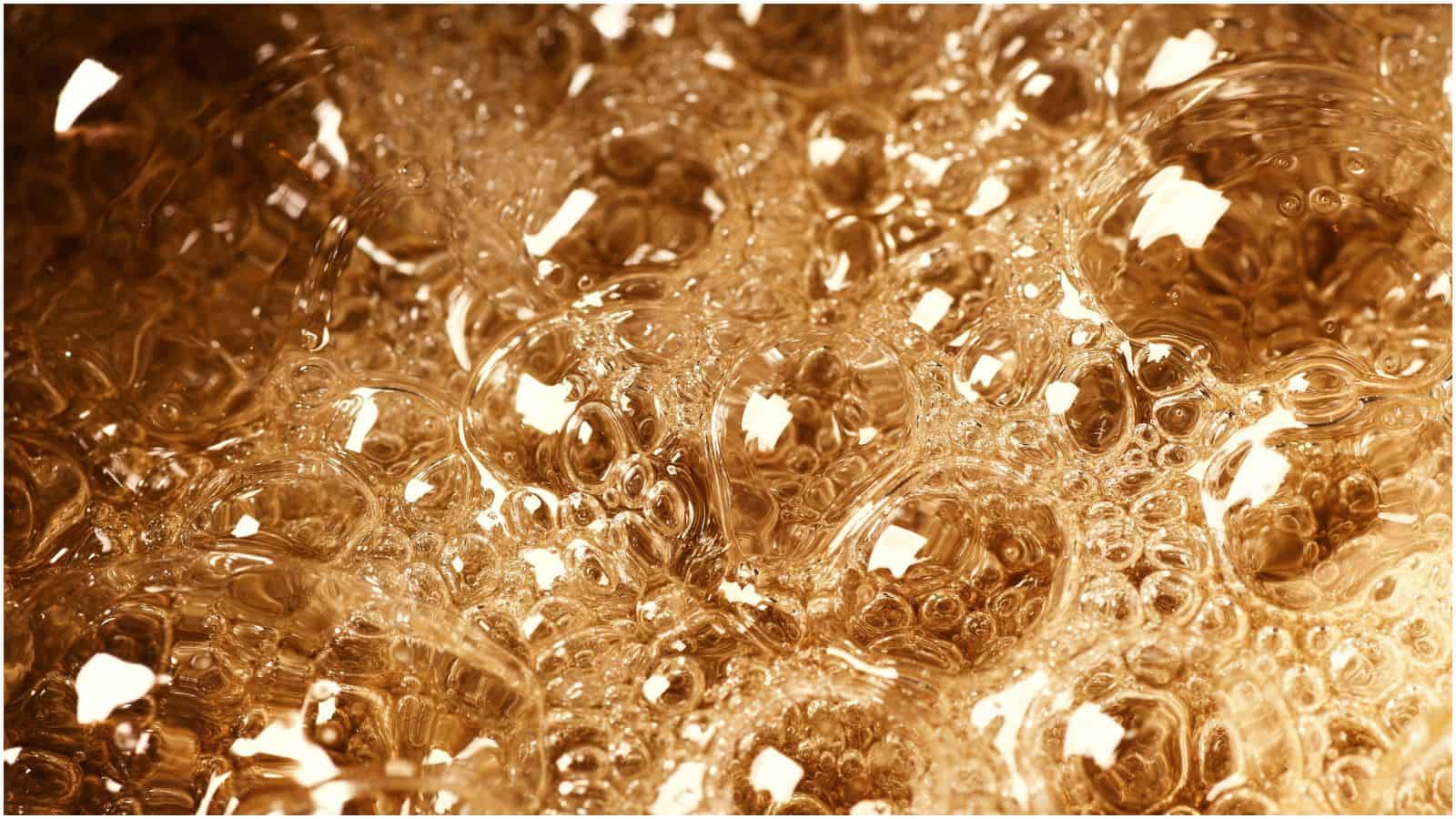 Close-up image of numerous overlapping, transparent bubbles with a golden-brown hue. The bubbles are tightly packed, casting reflections and creating a shimmery, intricate pattern&mdash;everything you need to know about simple syrup captured in this mesmerizing display.