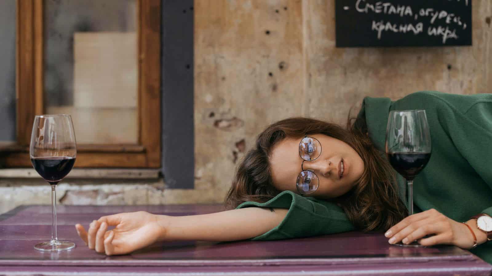 Woman lying down on a table with two glasses of wine found on top of it