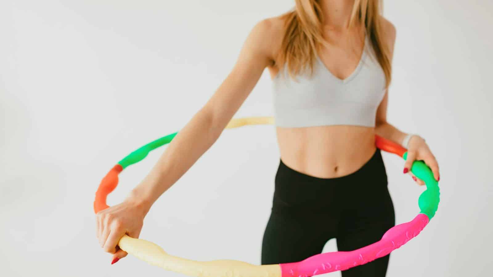 A person wearing a gray sports bra and black leggings is holding a colorful hula hoop. The image captures their torso and arms, but their face is not visible, as if they're preparing for a nighttime routine that includes lemon water before bed.