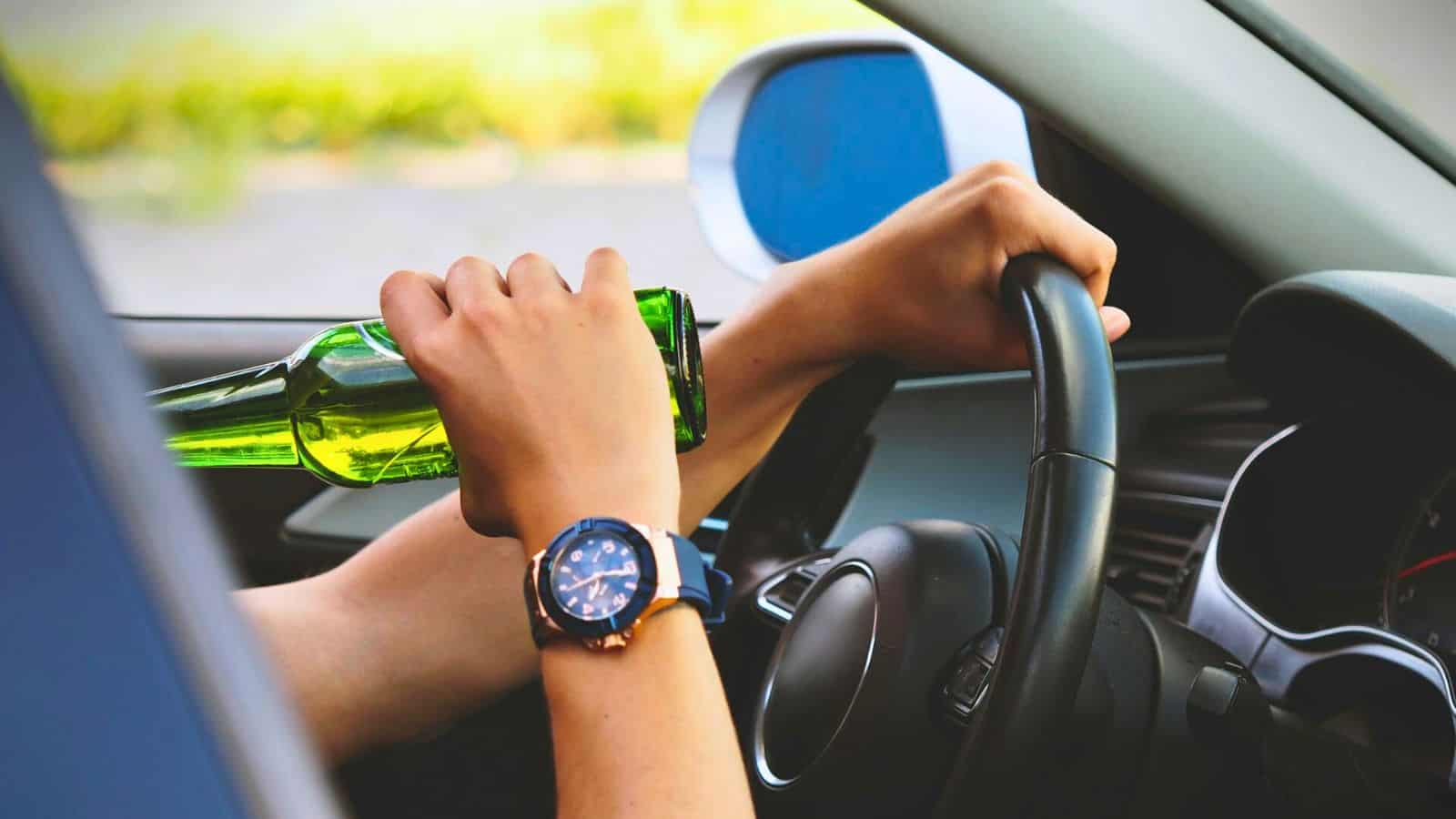 Person drinking a bottle of what seems to be alcohol while holding a steering wheel of the car
