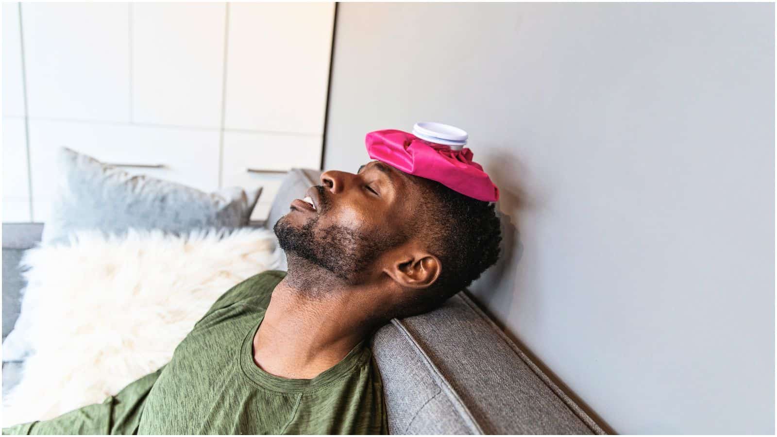 Man with a compress on his head lays on sofa