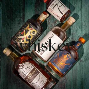 A display of whiskey bottles arranged on a dark green wooden surface. The word "whiskey" is overlaid in large text across the center of the image. There are five bottles from different brands, showcasing a variety of label designs and colors.