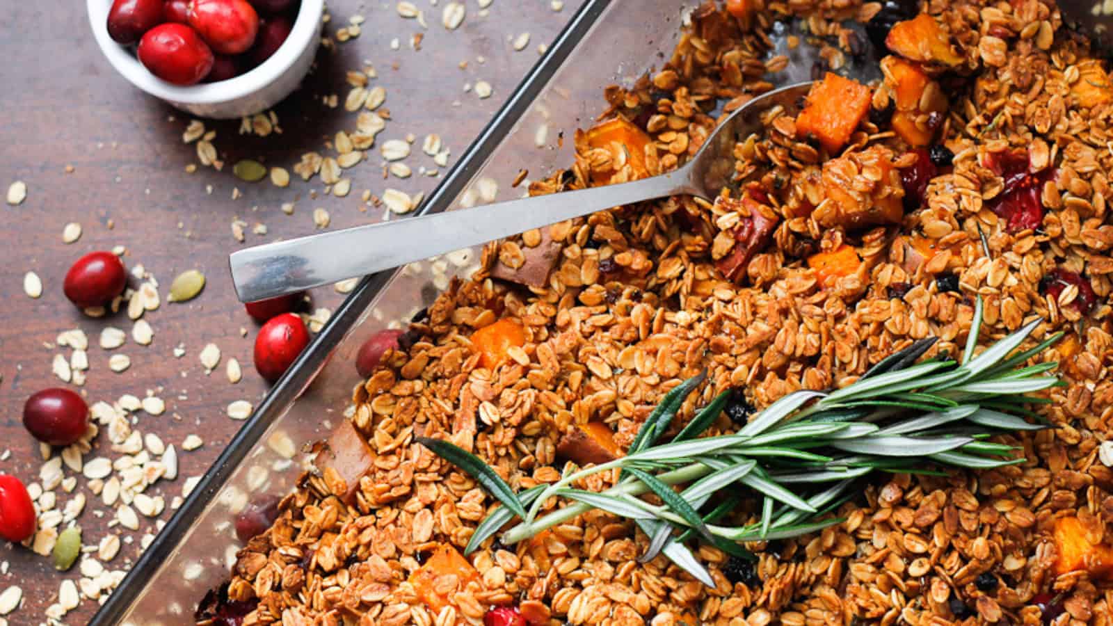 A dish of granola with cranberries and sprigs of rosemary.