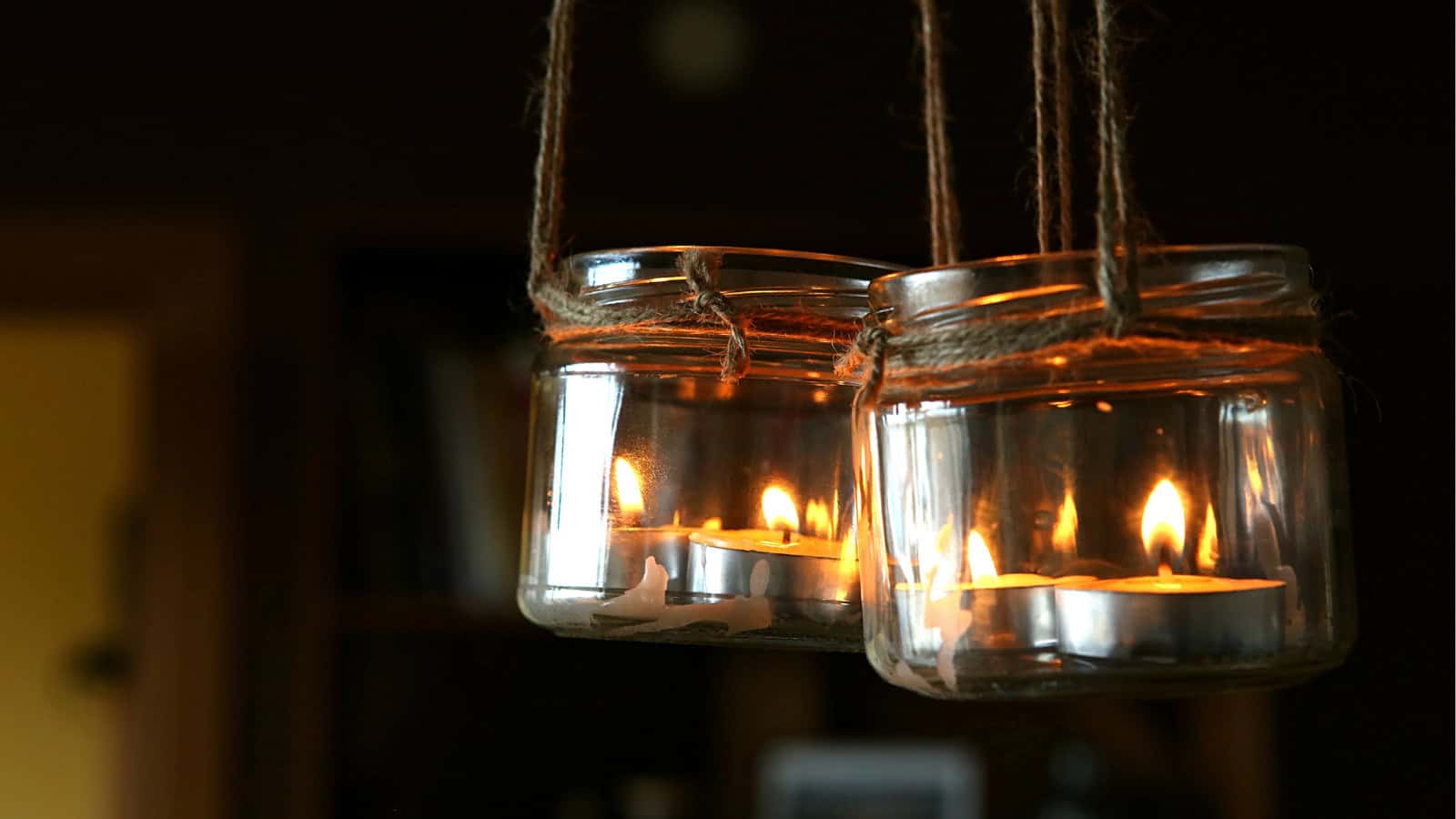 Two glass jars hang from strings with lit tea light candles inside, creating a soft, warm glow. The background is dimly lit, adding to the cozy atmosphere.