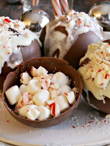 Four peppermint hot chocolate bombs on a plate, with an open hot chocolate bomb in the middle to show the inside.