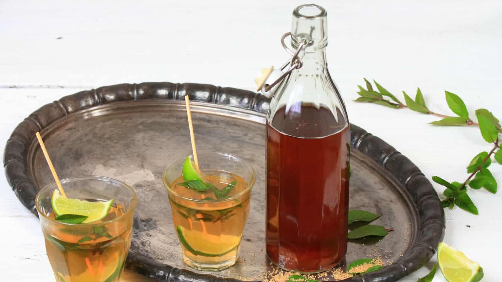 A picture of peppermint syrup and two drinks on the side on an oval metal tray.