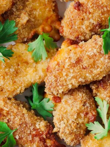 A plate of crispy breaded chicken strips garnished with fresh parsley.