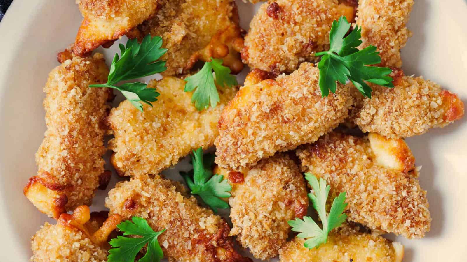 A plate of crispy breaded chicken strips garnished with fresh parsley.