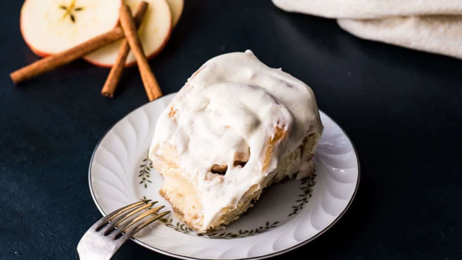 A pan of freshly baked and frosted apple cinnamon rolls on a dark blue background.