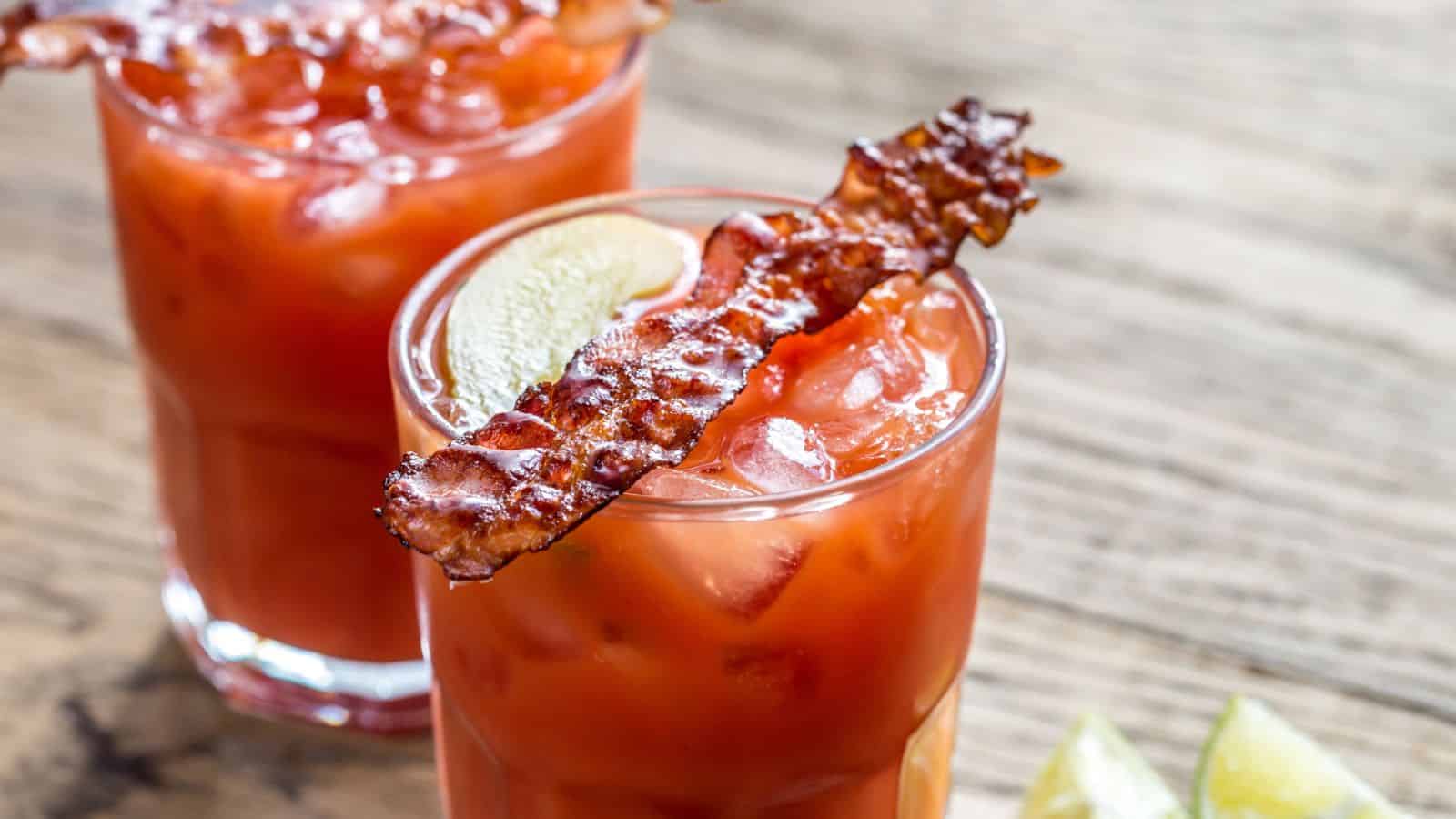 Two glasses of vodka with bacon on top of them.