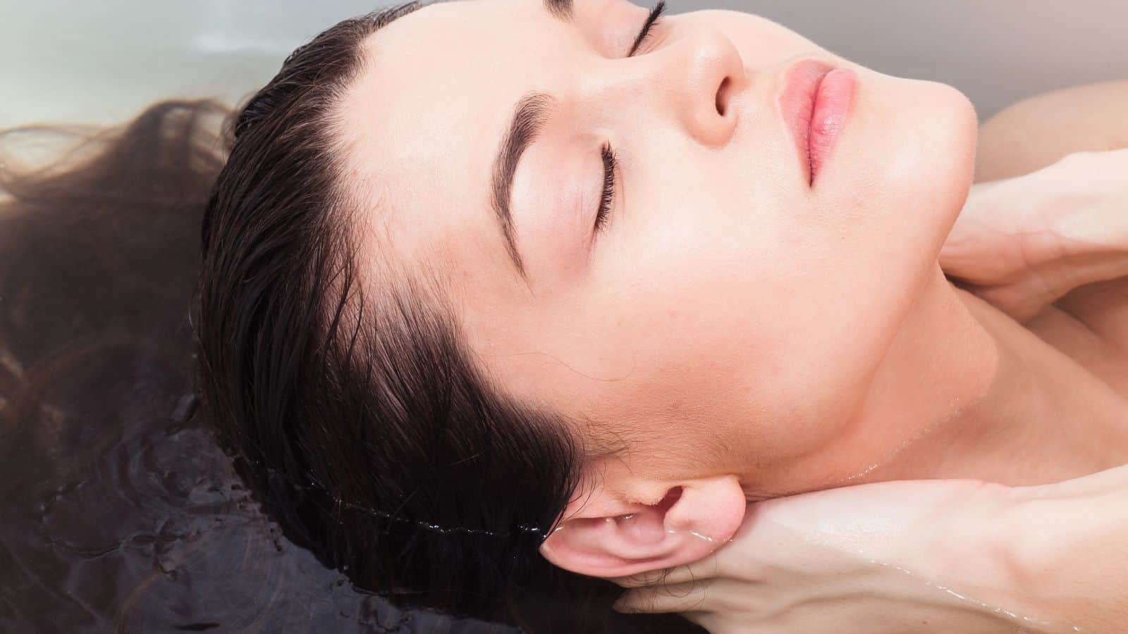 A person with closed eyes is partially submerged in water, their hands gently placed on their neck. The image focuses on the serene and relaxed expression of the individual, reminiscent of embracing surprising coffee grounds uses for a soothing escape.