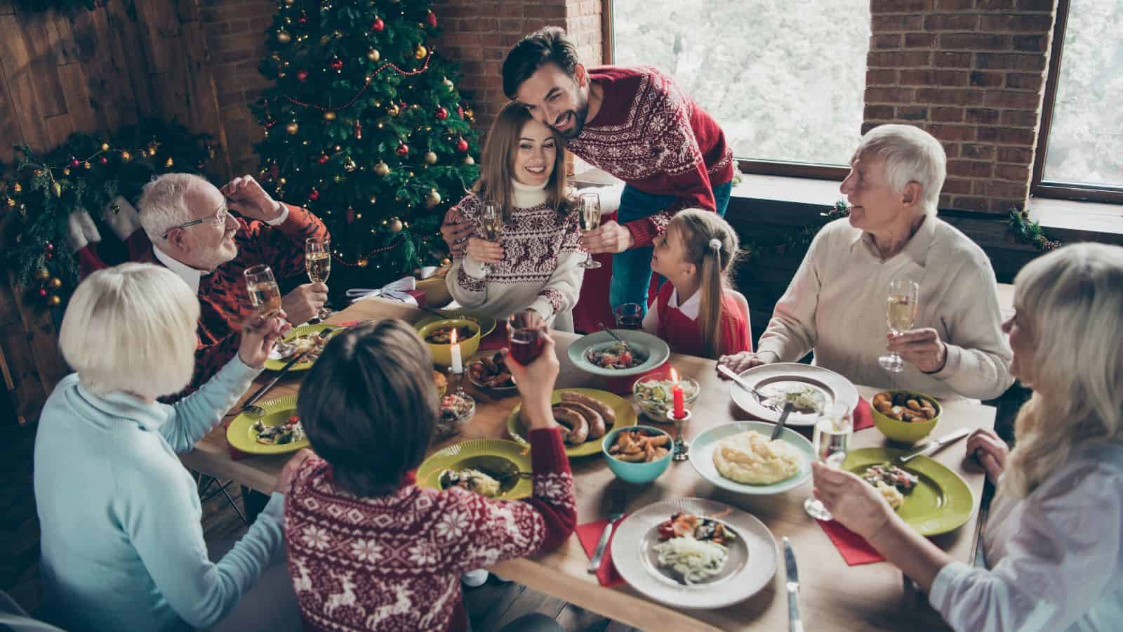A cheerful family gathered around a festive dinner table with a Christmas tree in the background, raising glasses in celebration.
