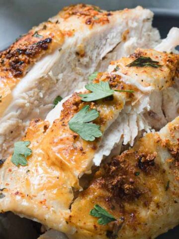 Grilled chicken pieces garnished with fresh parsley are served on a gray plate. A black and white checkered cloth is partially visible beside the plate.