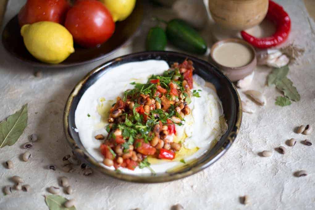 Dip on plate with tomatoes and spicy peppers around.